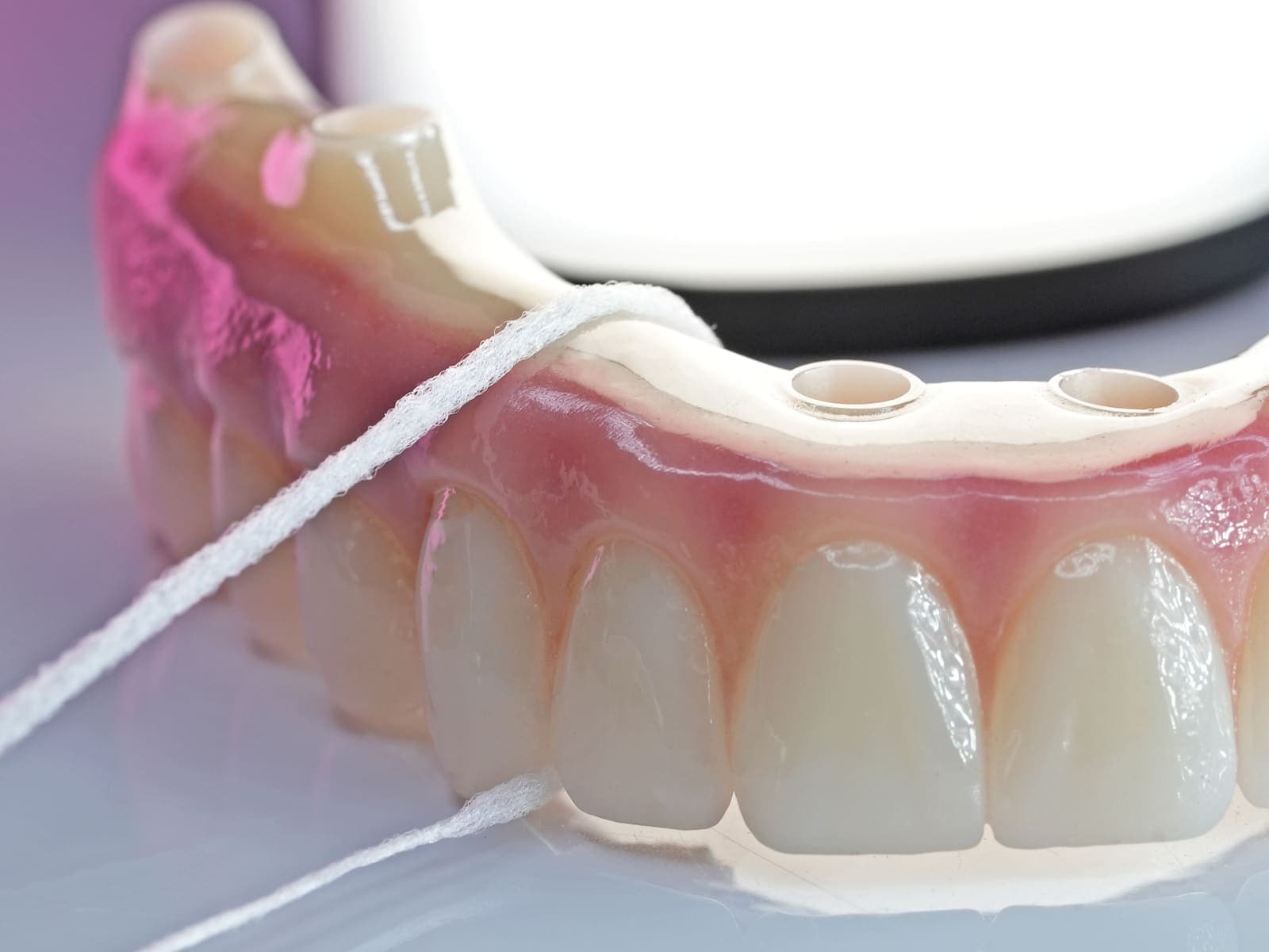 Floss passed under a finished full-arch prosthesis, showing the hygiene access