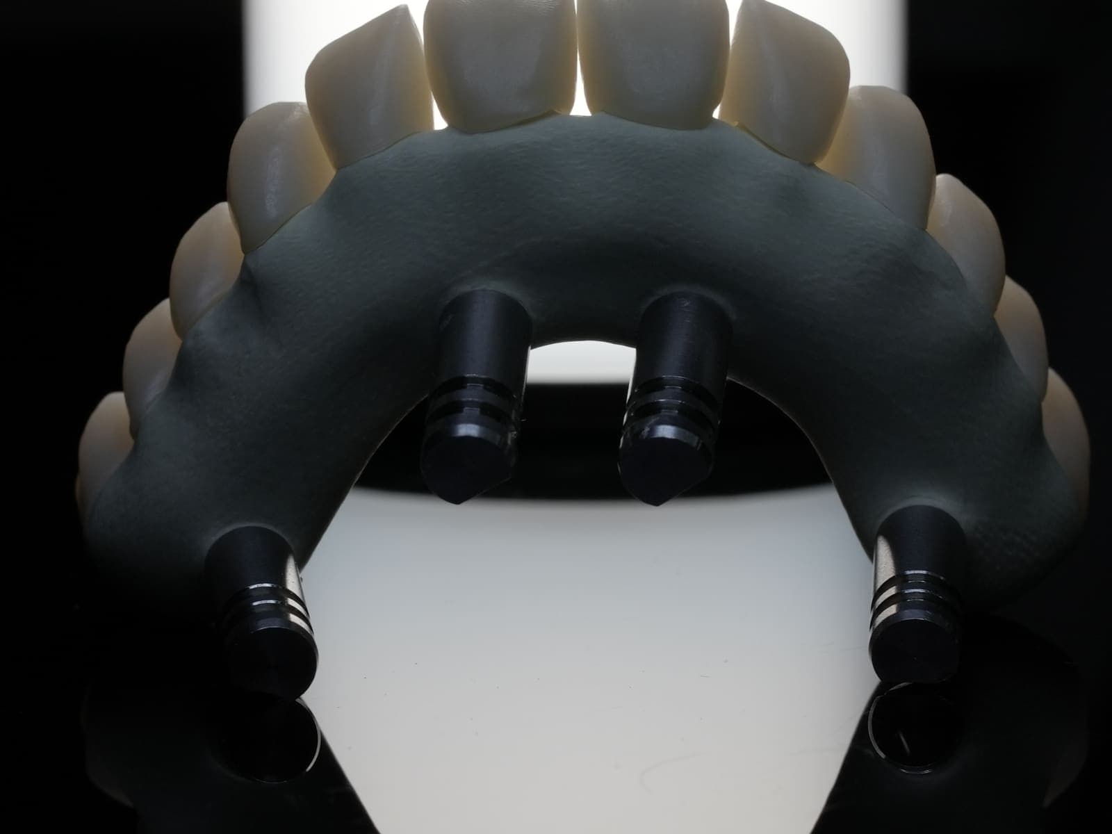 A full-arch prosthesis seated on its multi-unit abutments, photographed on black